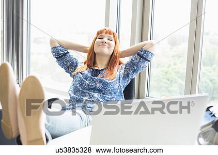 Stock Photo - Businesswoman relaxing with feet up at desk in creative office. Fotosearch