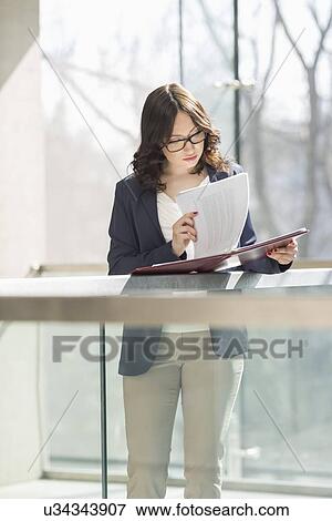 Businesswoman reviewing documents against railing in office View Large Photo Image Stock Photo - Businesswoman reviewing documents against railing in office. Fotosearch