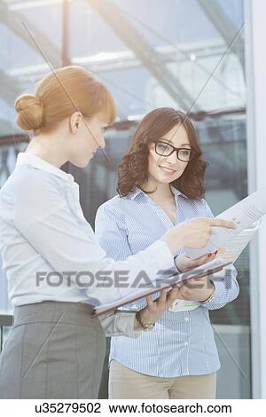 Stock Image - Businesswoman showing document to colleague in office. Fotosearch