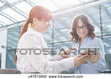 Businesswoman showing something on tablet PC to colleague in office View Large Photo Image Picture - Businesswoman showing something on tablet PC to colleague in office. Fotosearch