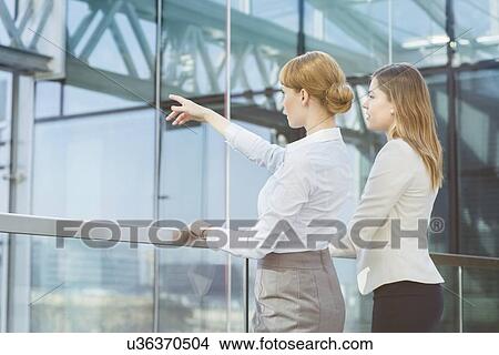 Businesswoman showing something to female colleague from glass wall in office View Large Photo Image Picture - Businesswoman showing something to female colleague from glass wall in office. Fotosearch