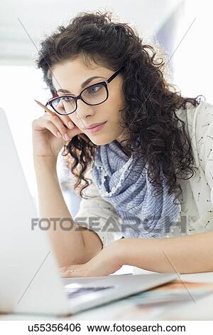 Stock Photograph - Businesswoman using laptop at desk in creative office. Fotosearch