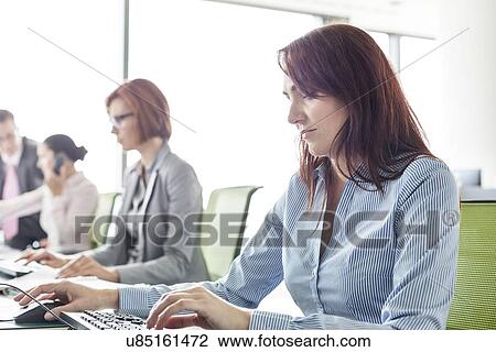 Stock Image - Businesswoman with colleagues working in open plan office. Fotosearch