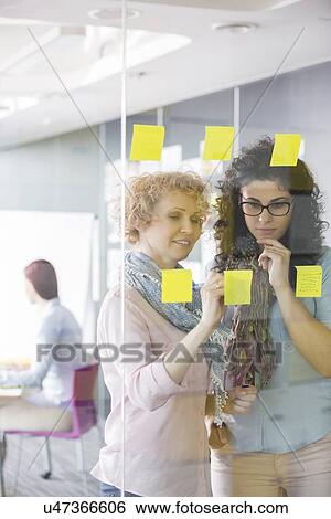 Businesswomen brainstorming with sticky notes in office View Large Photo Image Stock Photograph - Businesswomen brainstorming with sticky notes in office. Fotosearch