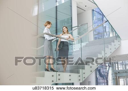 Stock Photography - Businesswomen conversing on steps in office. Fotosearch