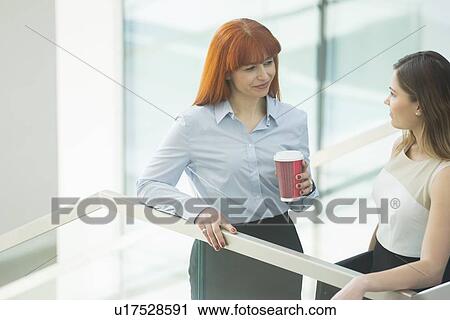 Stock Image - Businesswomen conversing while having coffee in office. Fotosearch