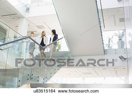 Picture - Businesswomen conversing while moving down steps in office. Fotosearch