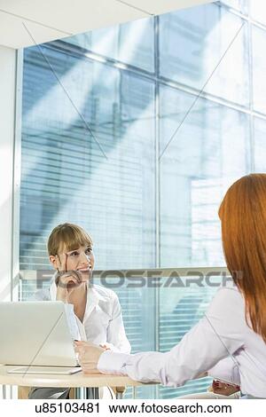 Stock Image - Businesswomen discussing at table in office. Fotosearch