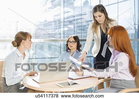 Businesswomen discussing over documents at table in office View Large Photo Image Stock Photo - Businesswomen discussing over documents at table in office. Fotosearch