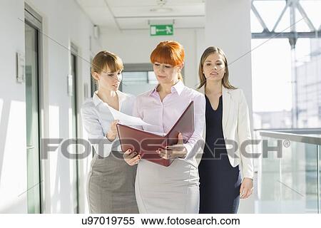 Businesswomen discussing over documents at office hallway View Large Photo Image Stock Photography - Businesswomen discussing over documents at office hallway. Fotosearch