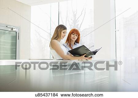 Picture - Businesswomen discussing over file folder in office. Fotosearch