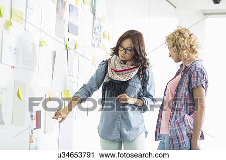 Businesswomen discussing over papers stuck on wall in creative office View Large Photo Image Stock Image - Businesswomen discussing over papers stuck on wall in creative office. Fotosearch