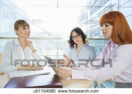 Stock Image - Businesswomen discussing over table PC at table in office. Fotosearch