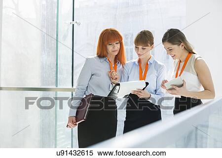 Stock Photography - Businesswomen doing paperwork by railing in office. Fotosearch