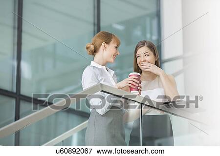 Businesswomen gossiping while having coffee on steps in office View Large Photo Image Stock Photo - Businesswomen gossiping while having coffee on steps in office. Fotosearch