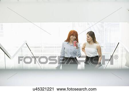 Stock Image - Businesswomen having coffee while moving up steps in office. Fotosearch