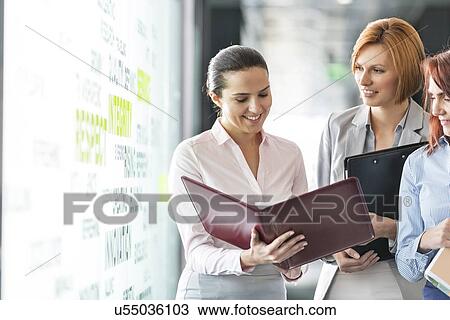 Stock Image - Businesswomen with file folders discussing in office corridor. Fotosearch