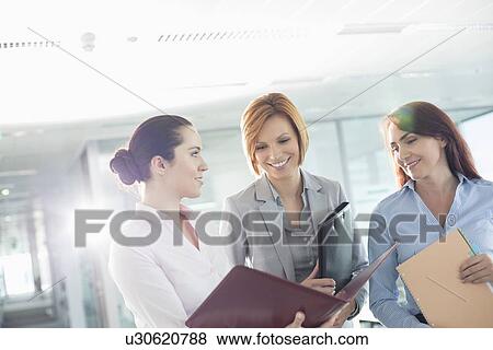Stock Photo - Businesswomen with file folders discussing in office. Fotosearch