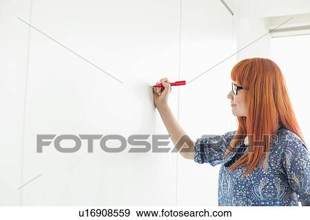 Stock Photo - Businesswomen writing on whiteboard in creative office. Fotosearch