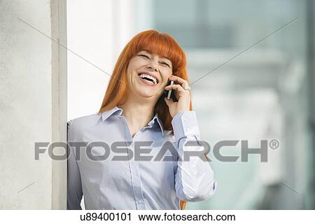 Stock Image - Cheerful businesswoman talking on cell phone in office. Fotosearch