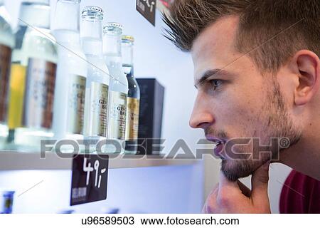 Close-up of man looking at beer bottles displayed on shelf in cafe View Large Photo Image Stock Image - Close-up of man looking at beer bottles displayed on shelf in cafe. Fotosearch