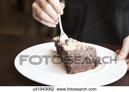 Stock Image - Close-up of woman's hand cutting chocolate pastry. Fotosearch