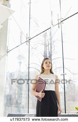 Confident businesswoman holding folder at office lobby View Large Photo Image Stock Image - Confident businesswoman holding folder at office lobby. Fotosearch