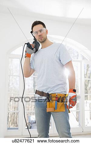Stock Image - Confident mid-adult man with drill in new house. Fotosearch