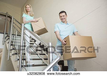 Couple carrying cardboard boxes while moving down steps at new home View Large Photo Image Stock Photo - Couple carrying cardboard boxes while moving down steps at new home. Fotosearch
