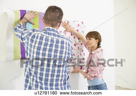 Stock Image - Couple holding up wallpaper samples in new house. Fotosearch