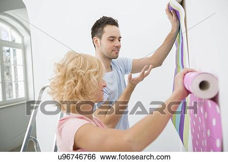 Stock Photograph - Couple holding up wallpaper samples in new house. Fotosearch