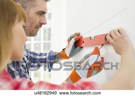 Stock Photo - Couple marking on wall with level in new house. Fotosearch