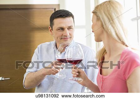 Couple toasting red wine glasses in kitchen View Large Photo Image Stock Image - Couple toasting red wine glasses in kitchen. Fotosearch