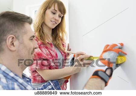 Couple using tape measure on wall View Large Photo Image Stock Photo - Couple using tape measure on wall. Fotosearch