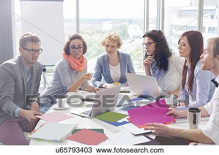 Stock Image - Creative business colleagues analyzing photographs at conference table in office. Fotosearch