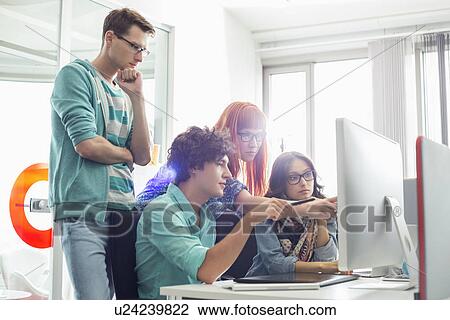 Stock Image - Creative business colleagues discussing over computer in office. Fotosearch