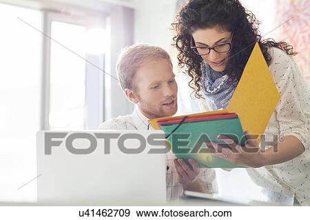 Stock Photo - Creative business colleagues discussing over file in office. Fotosearch