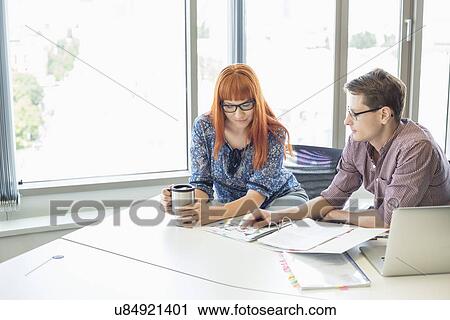 Creative business colleagues reading file together at desk in office View Large Photo Image Stock Image - Creative business colleagues reading file together at desk in office. Fotosearch