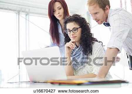 Stock Photo - Creative business colleagues using laptop at desk in office. Fotosearch
