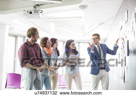 Stock Image - Creative businessman giving presentation to colleagues in office. Fotosearch