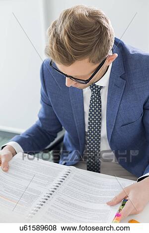 Creative businessman reading file at desk in office View Large Photo Image Stock Photo - Creative businessman reading file at desk in office. Fotosearch