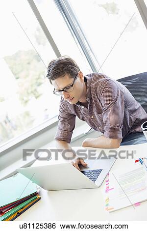 Stock Photograph - Creative businessman using laptop at desk in office. Fotosearch