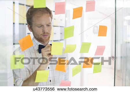 Stock Photograph - Creative businessman writing on sticky paper at office. Fotosearch