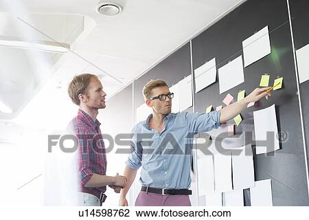 Creative businessmen discussing over sticky paper on wall in office View Large Photo Image Stock Image - Creative businessmen discussing over sticky paper on wall in office. Fotosearch