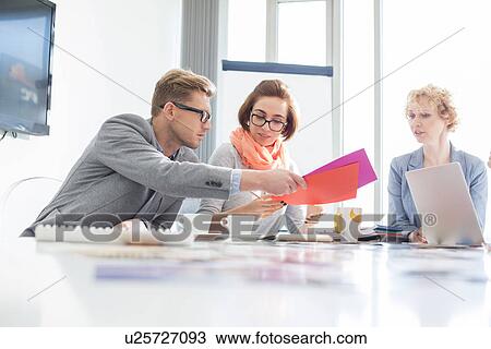 Stock Image - Creative businesspeople analyzing documents at desk in office. Fotosearch