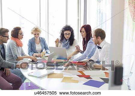 Stock Photography - Creative businesspeople analyzing photographs at conference table in office. Fotosearch