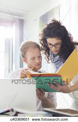 Stock Image - Creative businesspeople discussing over file in office. Fotosearch