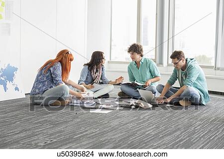 Picture - Creative businesspeople discussing while sitting on floor in office. Fotosearch