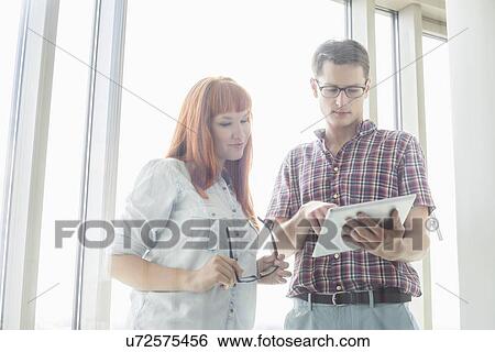Stock Photograph - Creative businesspeople using digital tablet together in office. Fotosearch