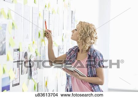 Picture - Creative businesswoman analyzing papers stuck on wall in office. Fotosearch